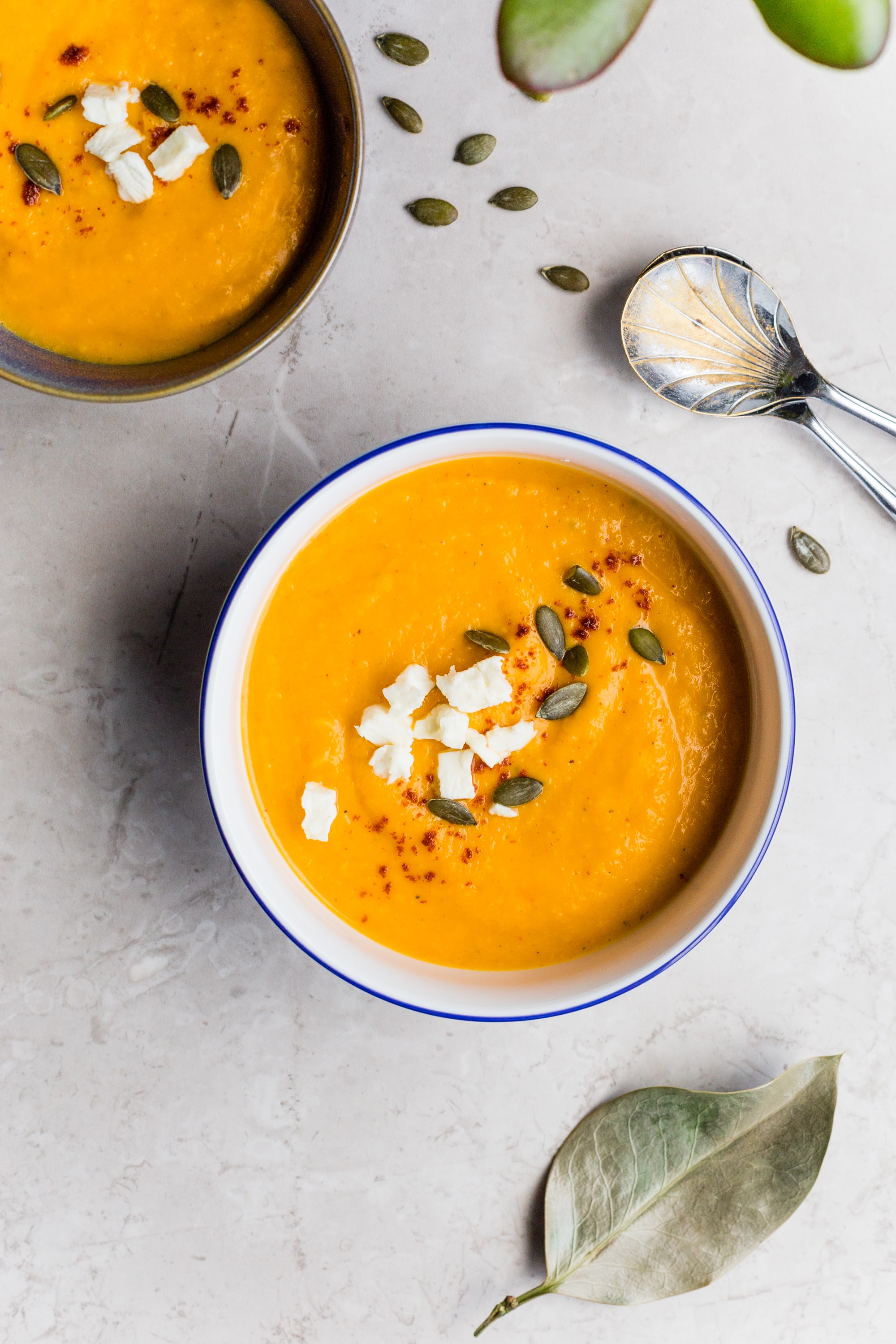 In two bowls, bright orange soup is garnished with pumpkin seeds