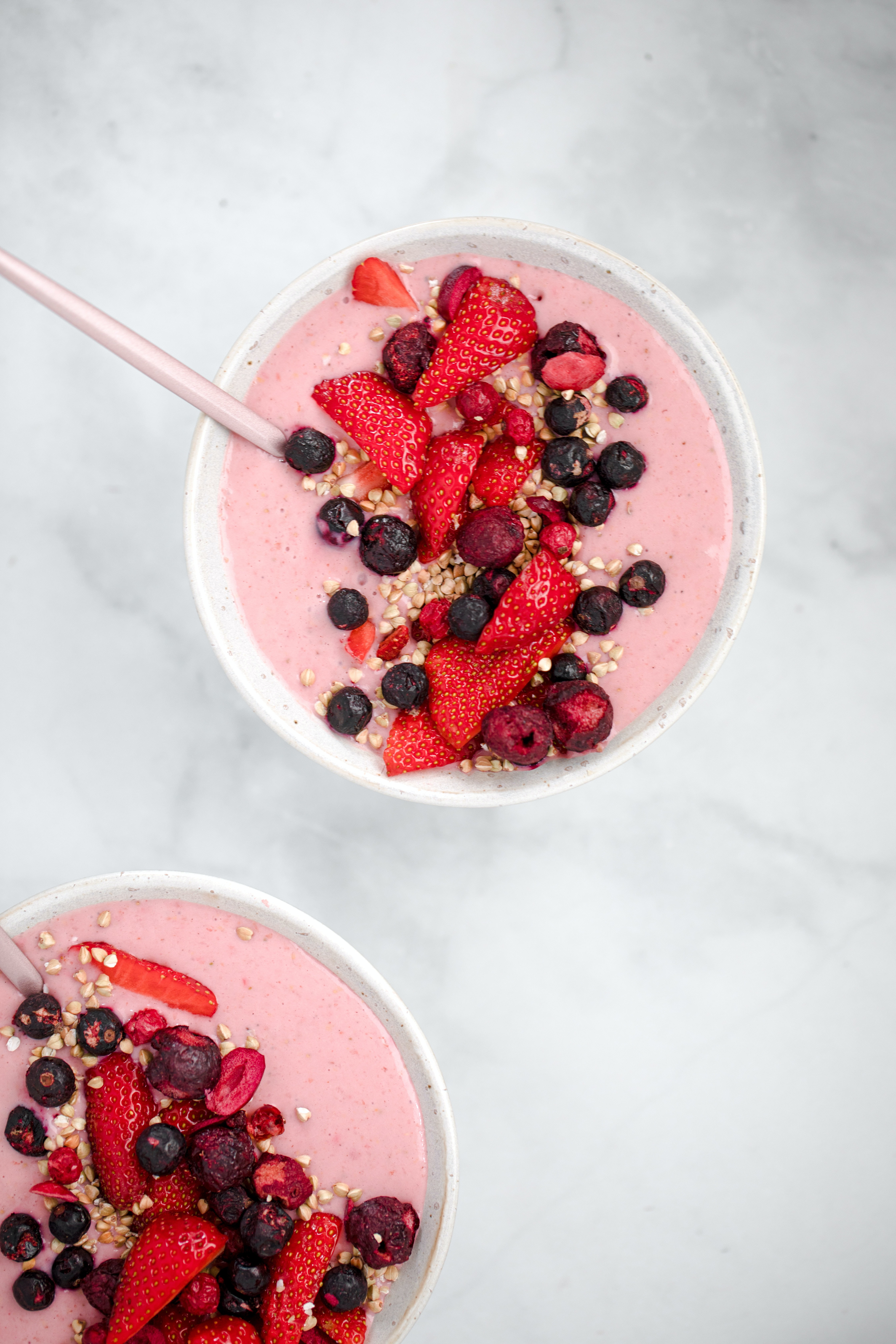 Two bowls full of a creamy pink substance are garnished by strawberries and blueberries